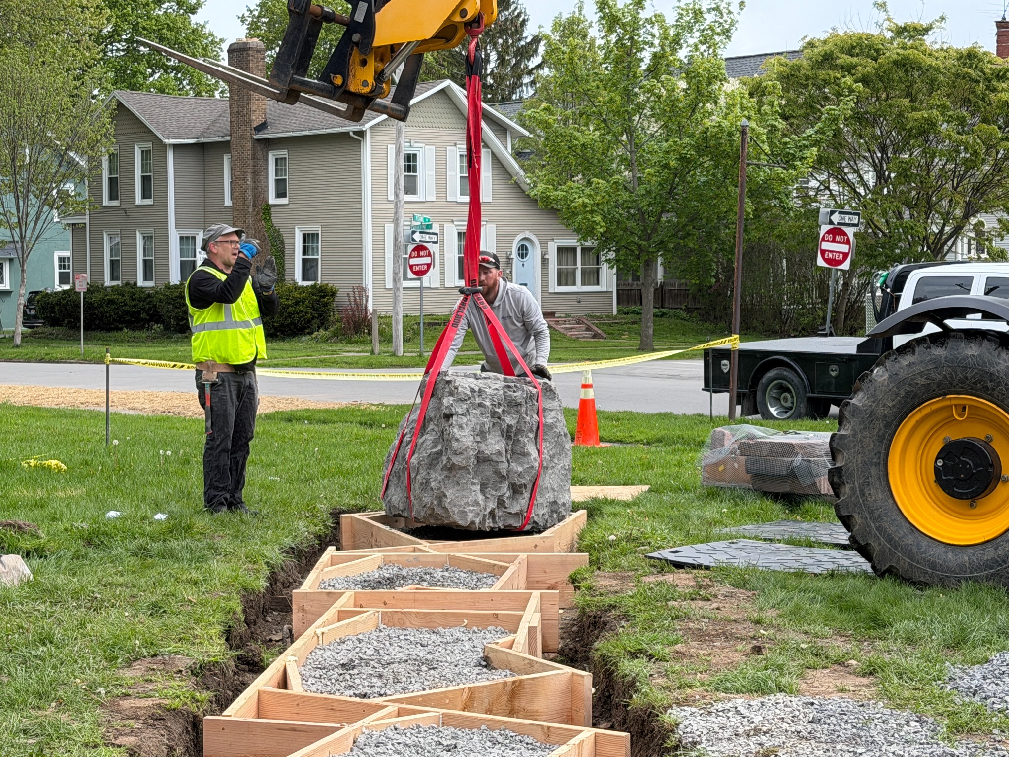 Crew guiding a stone into position with a telehandler during outdoor installation